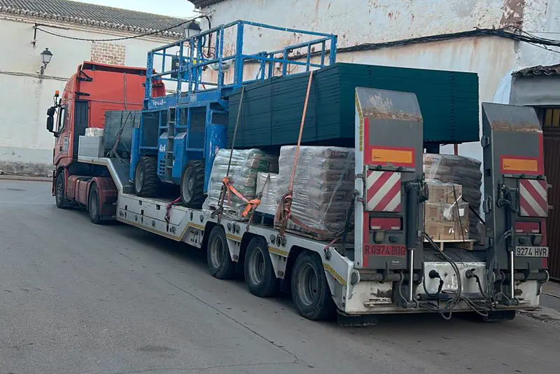 Góndola cargada con plataformas elevadoras y material paletizado.