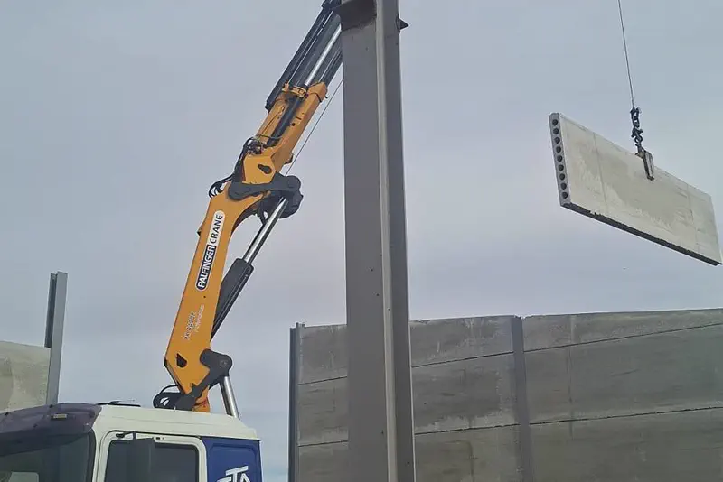 Pluma de Ayuso izando un panel de hormigón prefabricado en una obra.