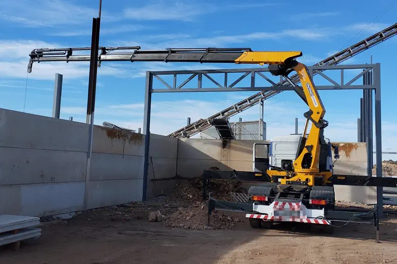 Camión pluma colocando la estructura metálica de una nave industrial en construcción.